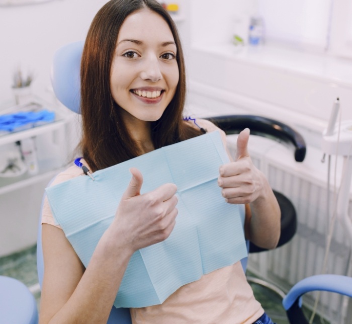Woman in dental treatment chair giving two thumbs up