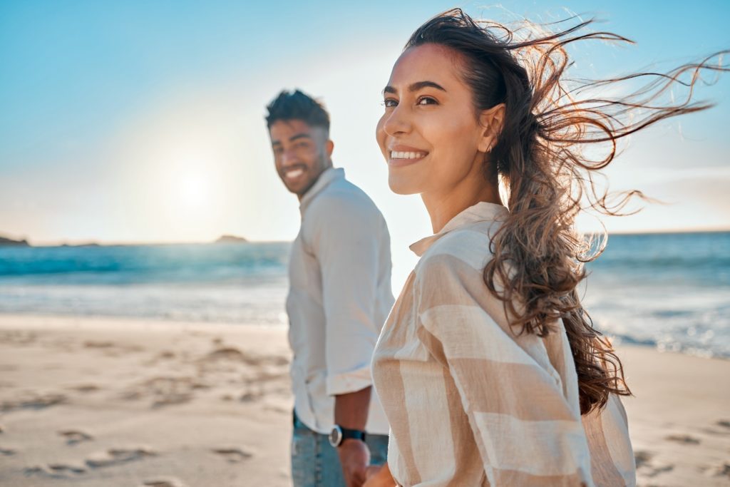 Couple smiling while holding hands and walking on the beach