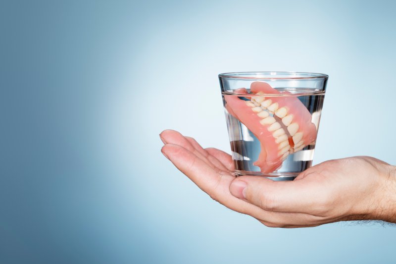 Dentures in glass of water resting in palm of someone's hand
